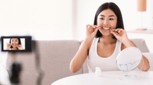 young asian lady using dental floss recording vlog DKWBCU3